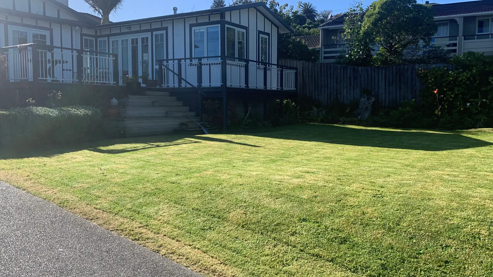 Wide front lawn mowed in front of a house with a timber deck
